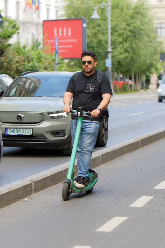 Man riding a green Bolt electric scooter down a city street